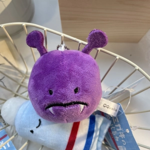 Close-up of a purple plush monster keychain with embroidery detail and metal chain