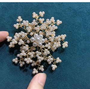 Detailed close-up of a gold flower brooch with white pearls against dark fabric