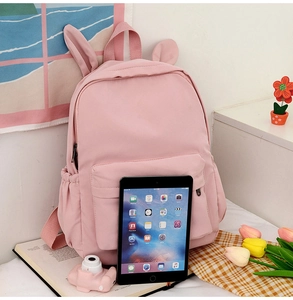 Pink student backpack with rabbit ears shown next to a tablet to demonstrate large capacity