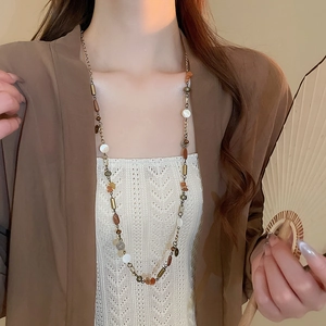 Dettaglio di una collana lunga vintage con perline, monete retrò e nappine stile boho