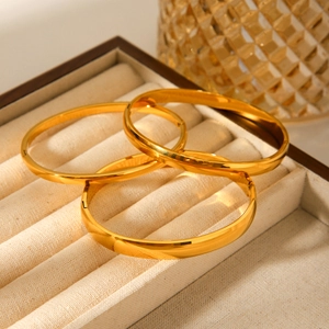 Three gold-plated stainless steel bangles showcased on a beige velvet jewelry display box