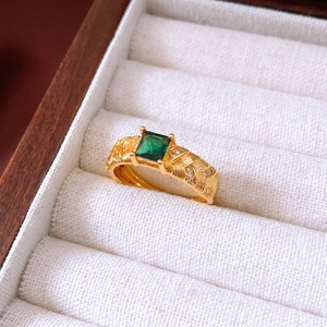Nahaufnahme eines Vintage-Goldrings mit quadratischem grünem Edelstein und Webstruktur