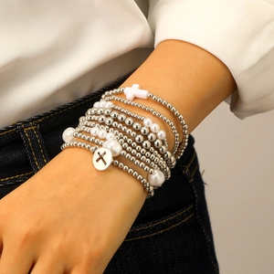 Dettaglio di set di braccialetti di perline a strati con perle argentate e ciondolo a croce