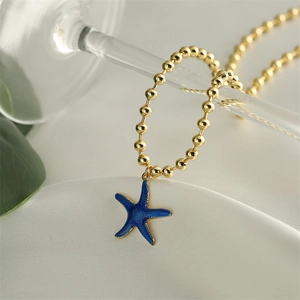 Macro shot of gold-plated beaded chain necklace with blue starfish pendant charm