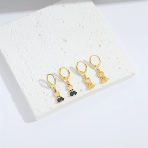 Macro view of dainty golden earrings with colorful zircon butterfly and doll charms