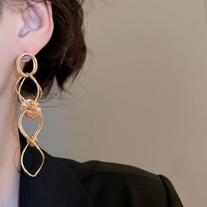 Model wearing gold geometric tassel drop earrings with layered twisted ring design