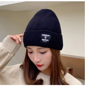 Detail of black knitted beanie featuring a square logo patch with white letter embroidery