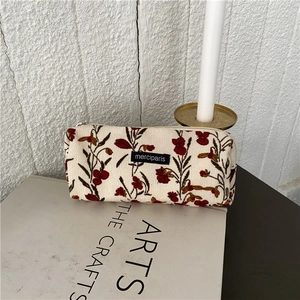 Detail view of cream corduroy makeup bag with floral embroidery on art books