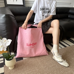 Detailed shot of pink canvas tote bag with red Sunday print in a cozy home setting