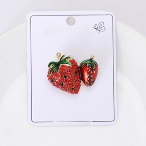 Detail of red rhinestone strawberry brooch with green enamel leaves on white display card