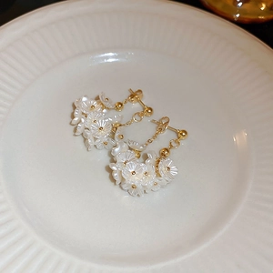 Elegante Blumenohrstecker mit weißen Blüten und Golddetails auf einem weißen Keramikteller