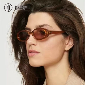 Close-up of model wearing oval amber sunglasses with brown lenses and metal hinge details