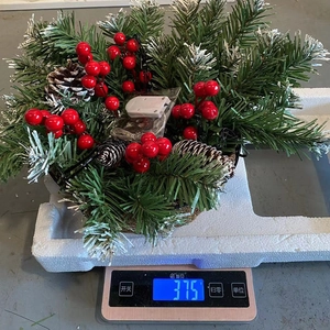 Detailansicht eines künstlichen Weihnachts-Hängekorbs mit Beeren und Zapfen auf einer Waage