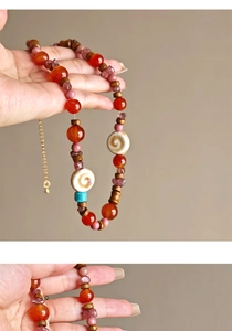 Detail of beaded necklace with red agate, wood, and turquoise stones on a gold chain