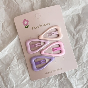 Detail of four heart-shaped metal hair clips in pink and purple on a fashion card