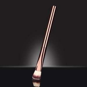 Detail of rose gold makeup brush with gradient bristles on reflective black surface