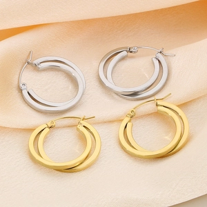 Crossed hoop earrings in gold and silver finish resting on soft beige silk fabric