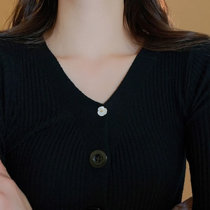 Detailed close-up of a flower brooch on a black ribbed knit cardigan with V-neckline