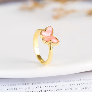 Macro shot of an adjustable butterfly ring in golden finish with pink inlay and bead edge