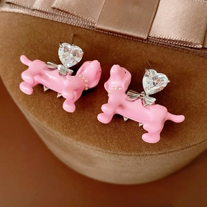 Macro detail of pink dachshund earrings with heart zircon and bow on velvet stand