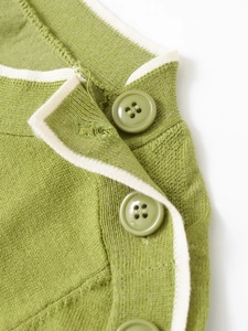 Detail of green knit sweater showing decorative shoulder buttons and contrast piping