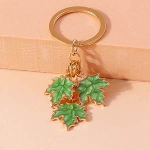 Close-up of golden keychain with green enamel ginkgo leaf pendants on a warm background