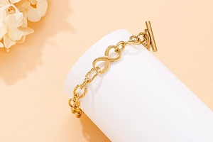 Detail of gold infinity charm bracelet with textured links and toggle OT clasp closure