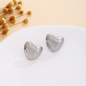 Detail of silver heart-shaped earrings with wave texture on a minimalist tray