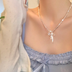 Detail view of a silver bow pearl necklace worn on a model with a soft knit sweater