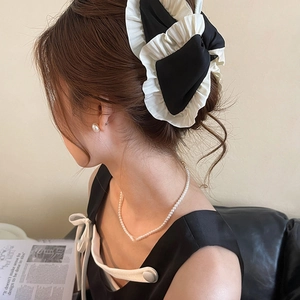 Detail of a black and white ruffled bow hair clip worn by a model with pearl jewelry