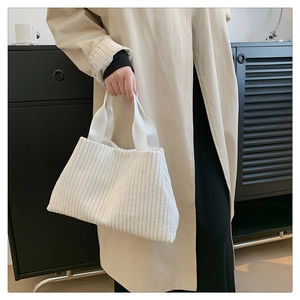 Close-up of white corduroy tote bag held by model featuring soft ribbed fabric texture