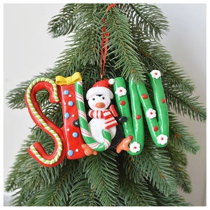 Close-up of polymer clay penguin SNOW charm hanging on a lush green Christmas tree branch