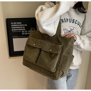 Detail of green corduroy tote bag featuring large front flap pockets and wide shoulder strap