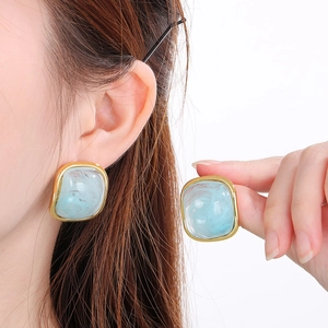 Détail d'une boucle d'oreille carrée en résine bleu clair avec bordure dorée sur modèle