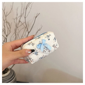 Mini floral cotton quilted cosmetic bag with blue bow detail held in hand for scale