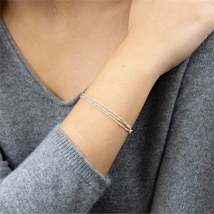 Detailed view of a three-layer silver beaded bracelet on a wrist with grey knitwear