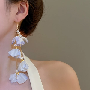 Détail de boucles d'oreilles fleurs en tissu lilas avec perles et longs glands dorés