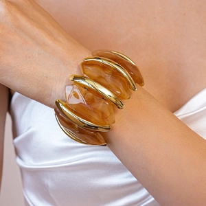 Gros plan d'un bracelet large en métal doré et blocs de résine ambrée au poignet