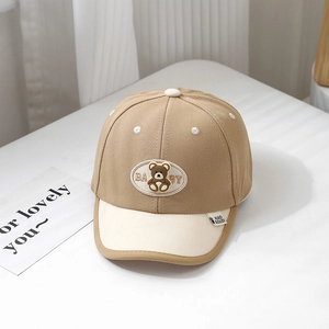 Detail of baby baseball cap with bear patch and embroidery on beige fabric