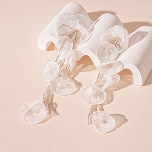 Macro shot of white handmade lace flower earrings with beaded tassels on stone base
