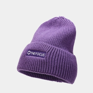 Close-up of purple knit beanie featuring thick ribbed texture and THE FOCUS patch label