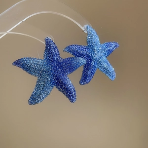 Macro shot of starfish earrings featuring blue gradient crystals on a minimalist stand