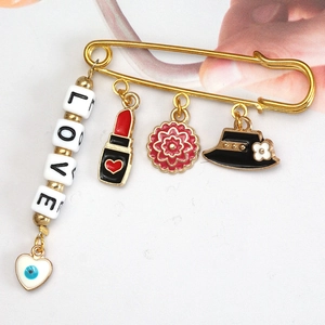 Detailed view of a gold safety pin brooch featuring LOVE beads and enamel charms