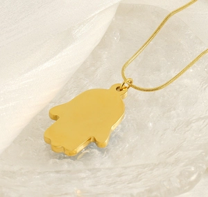 Close-up of golden Hamsa Hand pendant with snake chain on elegant white silk and glass