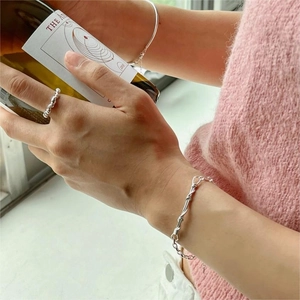 Detail view of 925 sterling silver knotted twist ring and minimal thin bracelets on wrist
