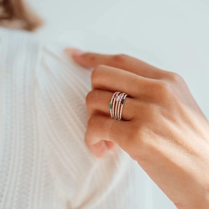 Close-up of five stacked gold rings with colorful square gemstones on a model finger
