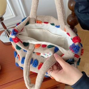 Close-up of beige plush tote bag interior with inner pocket and colorful pom-poms