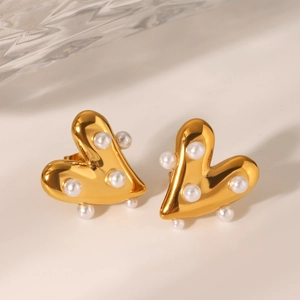 Vue macro des boucles d'oreilles cœur dorées 18K avec perles blanches sur fond épuré