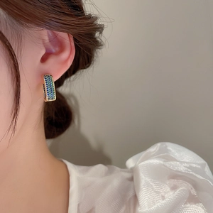 Close-up of gold huggie earrings featuring blue and green pave zircon geometric crystals