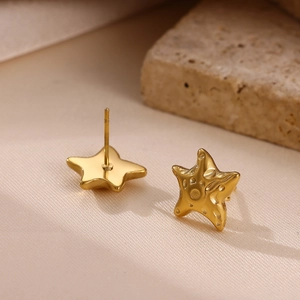 Gold starfish stud earrings with textured metallic finish on a minimalist stone background